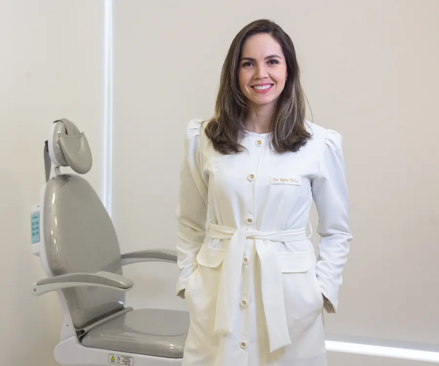 Dra. Rejane Pacheco de jaleco, sorrindo, no consultório
