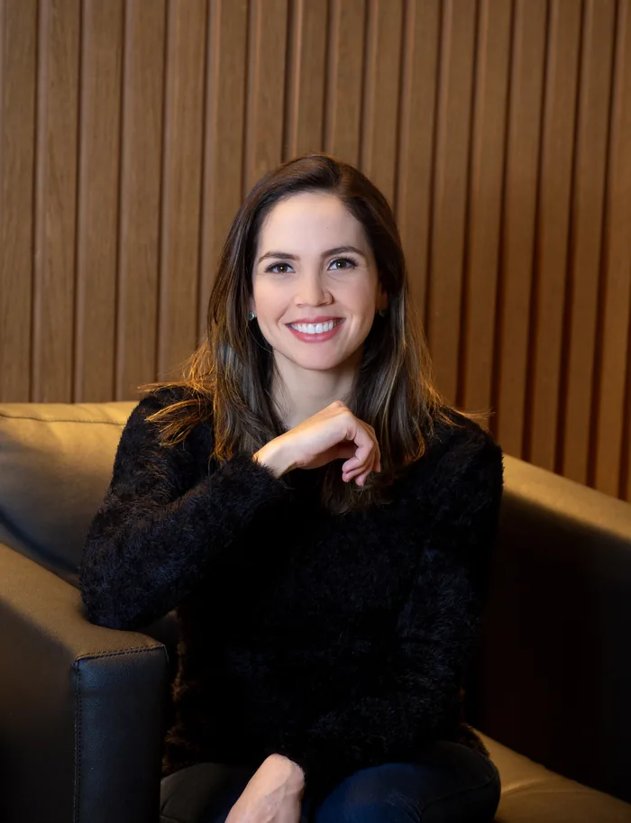 Dra. Rejane Pacheco sorrindo, sentada diante de um painel de madeira